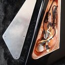 Fotografie zachicuje vnitřek elektroniky černé kytary a přilehlý k ní kovový kryt. V dutině těla je vidět měděné stínění, rozvedené elektrické kabely…