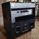 Černý basový kombo zesilovač v robustním kufrovém provedení s kolečky. Na horní části je bílý nápis BA300-210 a logo Ampeg. Zadní panel obsahuje ovlá…