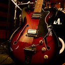 Polodupatá elektrická kytara s červeným gradientem (sunburst) a černým pickguardem. Kytara má dva humbuckery, dvě ovládací knoflíky a hnízdový most.…
