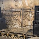Dva páry černých reproduktorových beden umístěných na dřevěných paletách. Horní bedna vpravo má v horním rohku červené logo JBL. Povrch všech beden j…