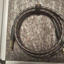Šedý pletený instrumentní kabel s oranžovými protkanými vlákny a zlatými konektory. Kabel je svinutý do kruhu a sevřený černým suchým stahovadlem. Na…