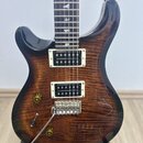 Elektrická kytara s tmavým plamenovým javorovým povrchem a dvěma humbuckery v bílých rámečcích. Na hrazdici jsou viditelné pětielové vložky ve tvaru…