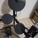 Elektronická bicí souprava s černými pady a činely. Na horním činely je viditelné logo YAMAHA, na ovládacím modulu nápis Roland a označení TD-1. Soup…