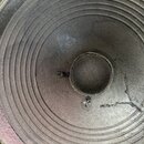 Fotografie zachycuje detail reproduktorového membrány v černé barvě. V pravé části je viditelná trhlina v materiálu membrány. U středu jsou patrné dv…