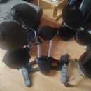 Elektronická bicí souprava s černými padmi a činely. Souprava je umístěna na černém kovovém stojanu s bílými podpěrnými trubkami. V horní části jsou…
