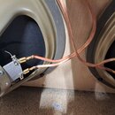 Detail vnitřku reproduktorové skříně s dvěma reproduktory v béžovém rámu. K terminálům jsou připojeny měděné vodiče s koncovkami. Na levém reprodukto…