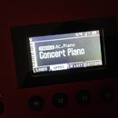 Detailní záběr na displej červeného klavíru nebo syntezátoru. Na obrazovce je zobrazen nápis SINGLE Ac.Piano a Concert Piano, v horní části jsou údaj…