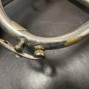Detail stříbrného dechového nástroje s viditelným mechanizmem klapky. Povrch je opotřebovaný, s několika škrábancemi a výrazným odloupením povrchové…