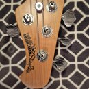 Fotografie zachycuje hlavu čtyřstrunné basové kytary z přírodního dřeva s chromovanými ladičkami. Na hlavě je černý nápis ERNIE BALL MUSIC MAN StingR…