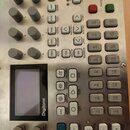 Stříbrný digitální syntetizátor s nápisem Digitone. Zařízení obsahuje několik šedých otočných knoflíků, displej a mřížku šedých tlačítek s čísly 1 až…