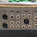 Zadní panel šedého zesilovače značky Peavey. Jsou zde viditelné vstupy a výstupy s nápisy MAIN LINE OUT, HEAD PHONES, CH 5 MONITOR INPUT, CHANNEL 4 I…