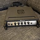 Černý basový zesilovač značky Ampeg s nápisem PortaFlex. Na horní straně je umístěno logo Ampeg. Přední panel obsahuje ovládací knofíky, přepínač -15…