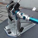 Detailní pohled na modrý a stříbrný bubnový pedál s řetězovým pohonem. Nástroj má černé gumové šlapky a stříbrné kovové části s viditelnou pružinou.…