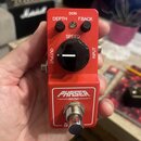 Červený kytarový efekt pedál s nápisem PHASER MINI. Na horní straně jsou dva malé černé otočné oválky s popisky DEPTH a F.BACK, velký černý ovládací…