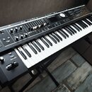 Černý elektronický klavír umístěný na černém stojanu. Na horním panelu je vidět nápis Roland Wunder a řada ovládacích prvků, včetně posuvníků, tlačít…