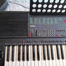 Černý digitální klavír s bílými a černými klávesami. Na předním panelu je uveden nápis YAMAHA PSR-400 a nad ním tabulka s označením zvuků. V pravé čá…