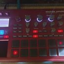 Červený sampler KORG electribe sampler MUSIC PRODUCTION STATION. Zařízení obsahuje displej s nápisem 001 Advisory 1 Part: 16 OSC Ride Hummy, několik…