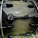 Detailní záběr na černý buben s kovovými obručmi a ladicími šrouby. Povrch nástroje má stříbrný glitrový efekt. Na korpusu je připevněn černý držák n…
