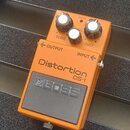 Oranžový kytarový efekt s nápisy Distortion DS-1 a BOSS. Na horní straně jsou tři ovládací knoflíky s popisky TONE, LEVEL a DIST oraz kontrolka CHECK…