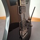 Detail elektrické kytary s černým lakovaným povrchem. Nástroj má dva humbuckery, tremolo mechanismus s páčkou a jeden viditelný ovládací knoflík. Na…