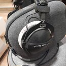 Černé sluchátka s bílými náušníky, položená na šedém textilním pouzdře. Na sluchátkách jsou viditelné nápisy beyerdynamic, 70 YEARS OF PASSION a thom…