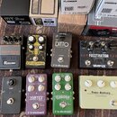 Fotografie zobrazuje skupinu sedmi kytarových efektů a jejich originální krabice. V horní řadě jsou pedály Boss Metal Zone MT-2w Waza Craft, Carcosa…