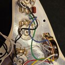 Fotografie zachycuje vnitřek elektroniky kytary s bílým povrchem a stříbrným stínováním. Jsou vidět tři potenciometry s nápisy 250K A 1836 a 250K A 4…