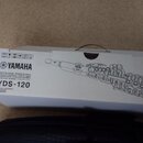 Bílá papírová krabice s černým potiskem. Na straně je logo a nápis YAMAHA, pod kterým jsou texty v několika jazycích a označení modelu YDS-120. Vedle…