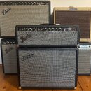 Fotografie zobrazuje čtyři kytarové komba. V horní části jsou dva zesilovače s nápisy Fender Deluxe Reverb Amp a Fender Harvard. Uprostřed stojí komb…
