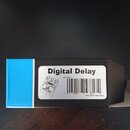Kartonová krabice s modrým bokem a bílou nálepkou. Na nálepce je nápis Digital Delay, kód O/N: 256817 a čárcový kód s číslem 568174. Vedle kódu je uv…
