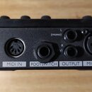 Zadávací panel černého elektronického zařízení s několika konektory. Jsou zde nápisy POWER, MIDI IN, FOOTSWITCH, OUTPUT a MIC INPUT. U napájecího vst…