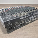 Šedý mixážní pult s velkým množstvím potenciometrů a přepínačů. Na boku je bílý nápis XENYX QX2222USB a logo behringer. Na zadní straně jsou viditeln…