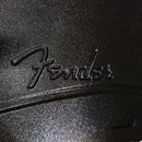 Detail černého plastového kufru s texturovaným povrchem. Uprostřed je vyembosované logo Fender. Povrch vykazuje mírné opotřebení a drobné škrábance.