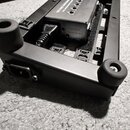 Černý kovový pedalboard s gumovými nožičkami. Uvnitř je umístěn stříbrný napájecí zdroj s nápisem ISO-2AC, SA600 a INPUT. Na boku pedalboardu je vidě…