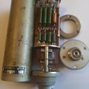 Fotografie zobrazuje rozebraný kondenzátorový mikrofon. Je zde vidět vnitřní elektronika s rezistory, transformátor a kovové šasi. Na spodní části vn…