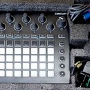 Černý sekvenční syntetizátor Novation CIRCUIT v dopravním pouzdře z pěnového materiálu. Zařízení má bílé podsvícené pady, několik otočných potenciome…