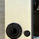 Detail stříbrného kovového šasi efektového pedálu. Jsou vidět dva vstupy: jeden 6,35mm jack a jeden trojpólový XLR konektor připevněný dvěma šrouby.…