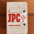 Kremovobílá DI box s kovovým šasi. Na horní straně je červené logo Radial engineering a velký červený nápis JPC MK3, pod kterým je text STEREO PC DI…