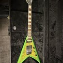 Zelená elektrická kytara s tělem ve tvaru V, položená v černém tvrdém kufru. Na hlavě je bílý nápis Jackson. Kytara má dva humbuckery, šest strun a h…