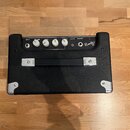 Černý basový kombo zesilovač s texturovaným povrchem a chromovanými rohy. Na ovládacím panelu jsou nápisy INPUT, VOLUME, BASS, MID, TREBLE, AUX IN a…