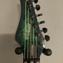 Hlava elektrické kytary v modro-zeleném mramorovaném provedení s černými ladičkami. Na povrchu je bílý nápis „Schecter Diamond Series“ a na hraně hla…