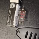 Krabice a elektronová trubice značky Electro-Harmonix. Na krabici je bílý nápis 12AU7/ECC82 electron tube a čárcový kód s označením HN133620. Skleněn…