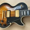 Elektrická kytara s tónem sunburst a černým plechtrákem. Nástroj má dva zlaté humbuckery, zlatý most a čtyři černé ovládací knoflíky. Na přepínači tó…