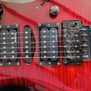 Detail elektrické kytary s červeným plamenovitým povrchem. Nástroj má tři černé humbuckery, z nichž na dvou je viditelný nápis EMGH Z. Kobylka je kov…