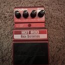 Červený kytarový efekt s černým pedalem. Na přístroji jsou nápisy HOT ROD ROCK DISTORTION a logo DigiTech. Obsahuje čtyři ovládací knoflíky s popisky…
