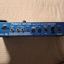 Zadní strana modrého kytarového syntetizátoru s nápisem Roland GR-55 GUITAR SYNTHESIZER. Jsou zde vidět různé konektory s popisky: GK IN, GUITAR OUT,…