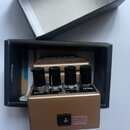 Zlatý efektový pedál v kartonové krabici. Na horní straně jsou čtyři černé ovrtovací knoflíky s popisky MODE, SENS, MANUAL a DECAY. Na přední straně…