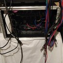 Otevřený hliníkový transportní kufr s černým vnitřním polstrováním, ve kterém je umístěno několik rackových zařízení. Z přístrojů vedou různé propojo…