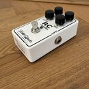 Bílý kytarový efekt pedál v kovovém šasi s černými ovládacími knoflíky. Na horní straně je nápis RC -booster a popisky VOLUME, BASS, TREBLE, INPUT a…