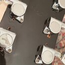 Záběr na zadní stranu černé hlavy kytary s chromovanými ladičkami. Povrch lakování vykazuje drobné škrábance a opotřebení v okolí otvorů pro ladičky.…